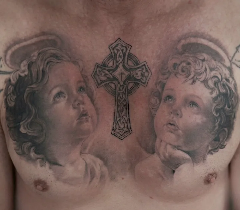 Dos querubines realistas mirando hacia una cruz celta, tatuados en el pecho