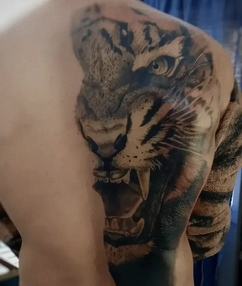Tigre realista con las fauces abiertas tatuado sobre el omóplato