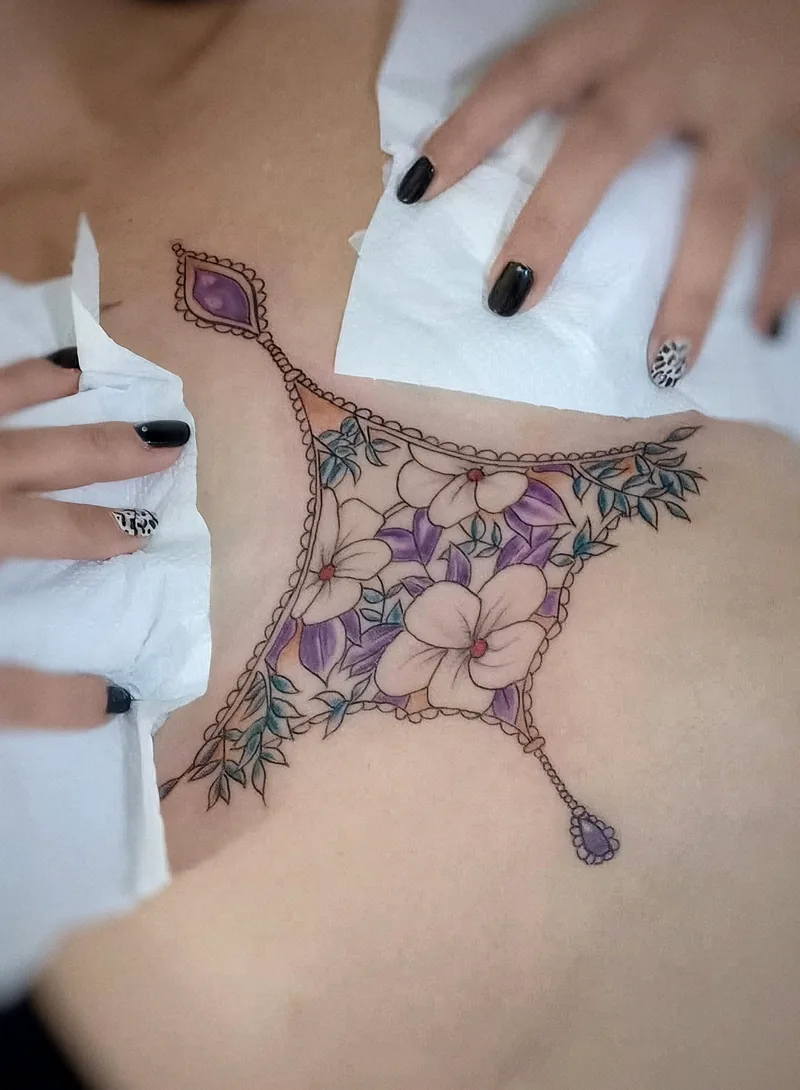 Ornamento floral en color con flores violetas y colgantes, tatuado bajo el pecho